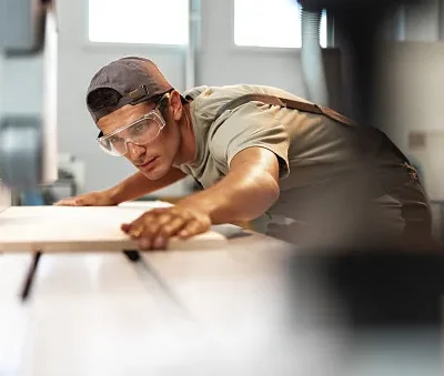 young carpenter cutting a piece of wood in using a circular saw in furniture factory