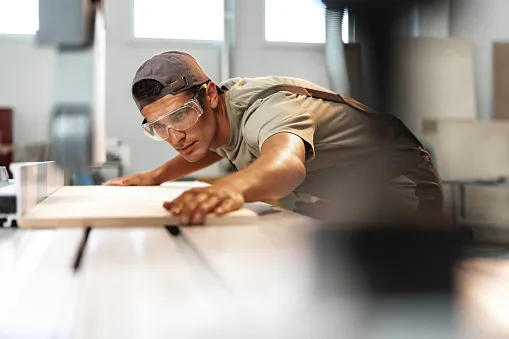 young carpenter cutting a piece of wood in using a circular saw in furniture factory